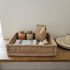 Handwoven willow shallow storage tray holding spice jars, a paper bag of coffee and garlic on a rustic wooden kitchen shelf