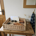 Shallow willow entryway tray on a hall table holding keys, sunglasses, a wallet, gloves and letters next to the front door
