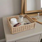 Handwoven wicker vanity tray holding cotton pads, a lipstick, a hair tie and cotton buds on a dresser in front of a mirror