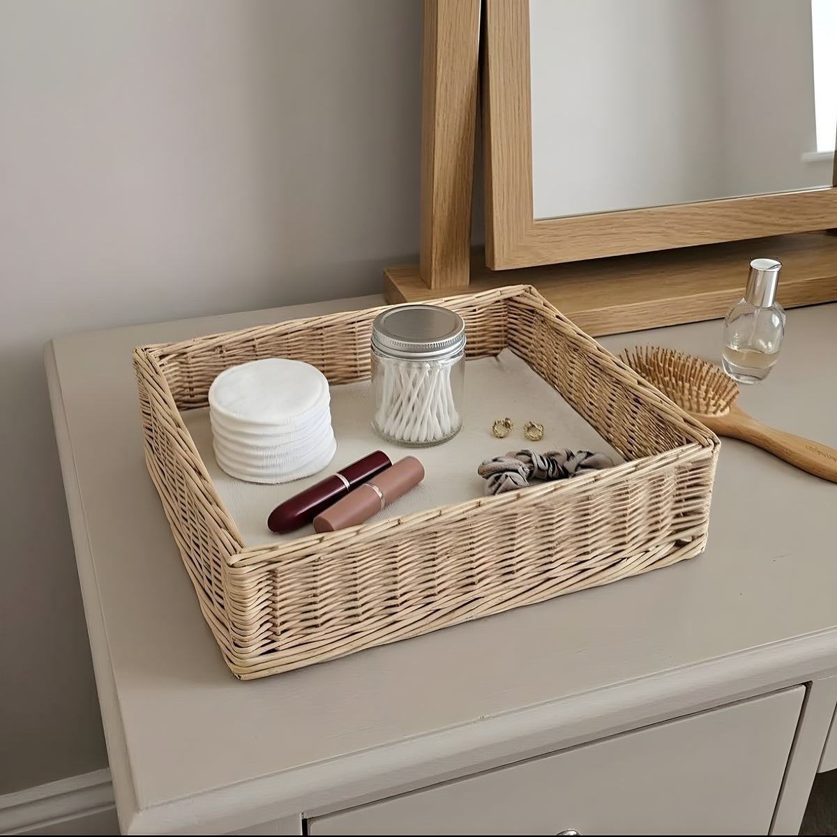 Handwoven wicker vanity tray holding cotton pads, a lipstick, a hair tie and cotton buds on a dresser in front of a mirror
