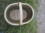 Top view into the large oval willow market basket on the grass, showing the woven oval base, braided rim and handle.