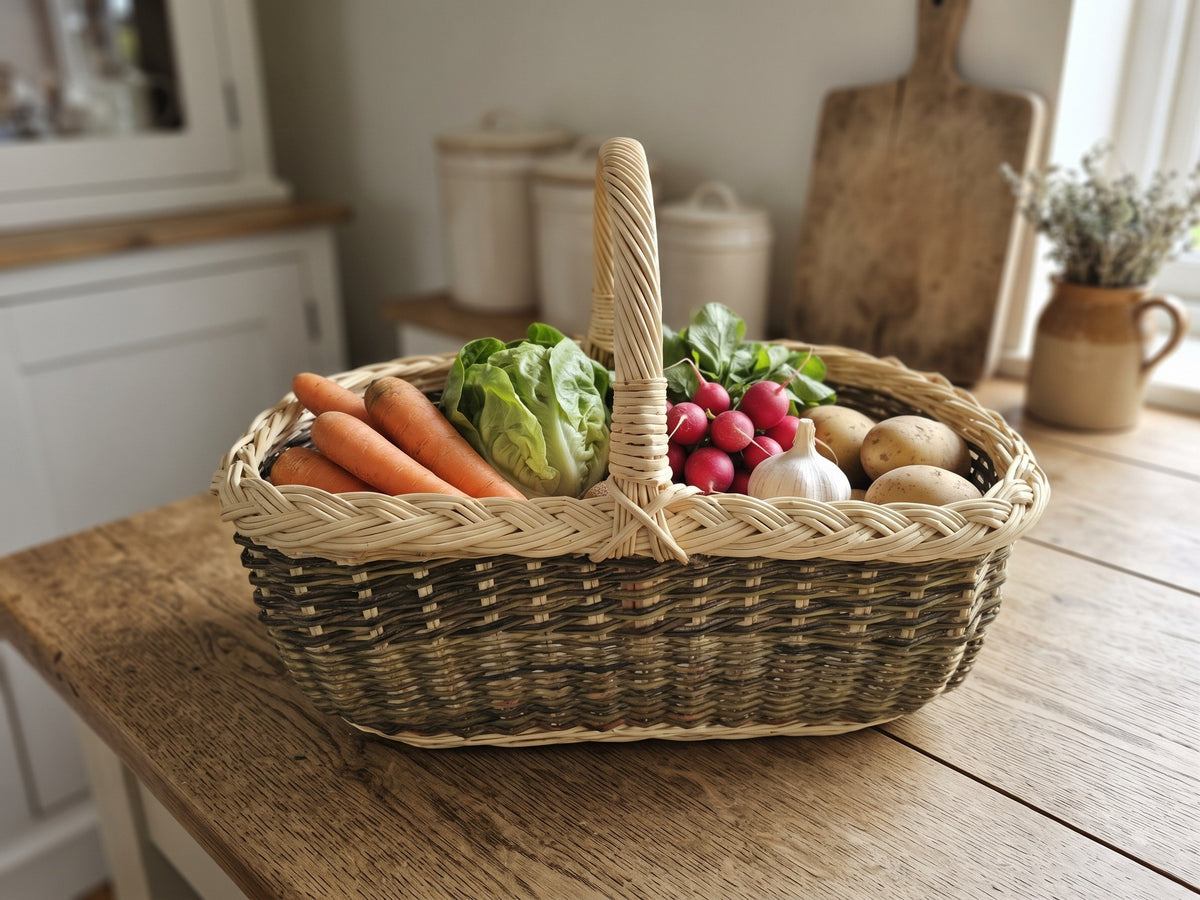 Handwoven willow market trug with a plaited rim holding carrots, lettuce, radishes and potatoes on a farmhouse kitchen counter
