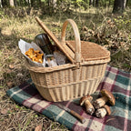 Weidenkorb mit Deckel und Henkel auf einer karierten Decke im Wald, eine Deckelhälfte offen, darin Pfifferlinge, eine Thermoskanne und Brot