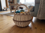 Round wicker basket with braided rim holding balls of yarn and knitting needles on a wooden floor in a cosy living room