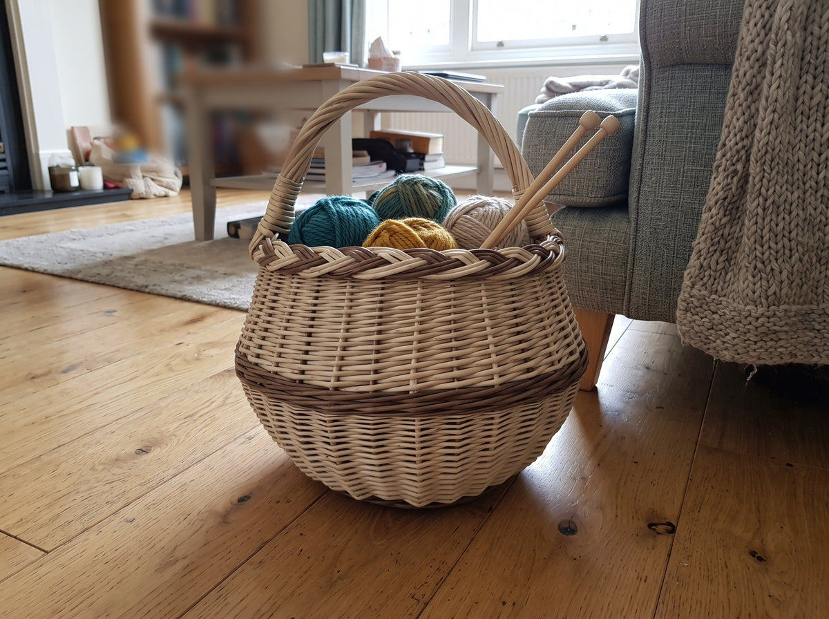 Round wicker basket with braided rim holding balls of yarn and knitting needles on a wooden floor in a cosy living room