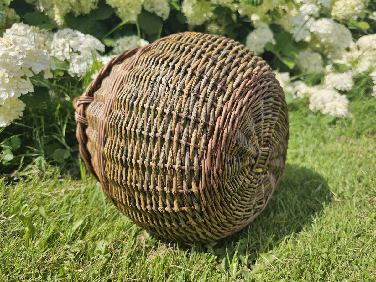 Side view of the small round willow basket lying on the lawn, showing the tight weave of its rounded body and the reinforced rim