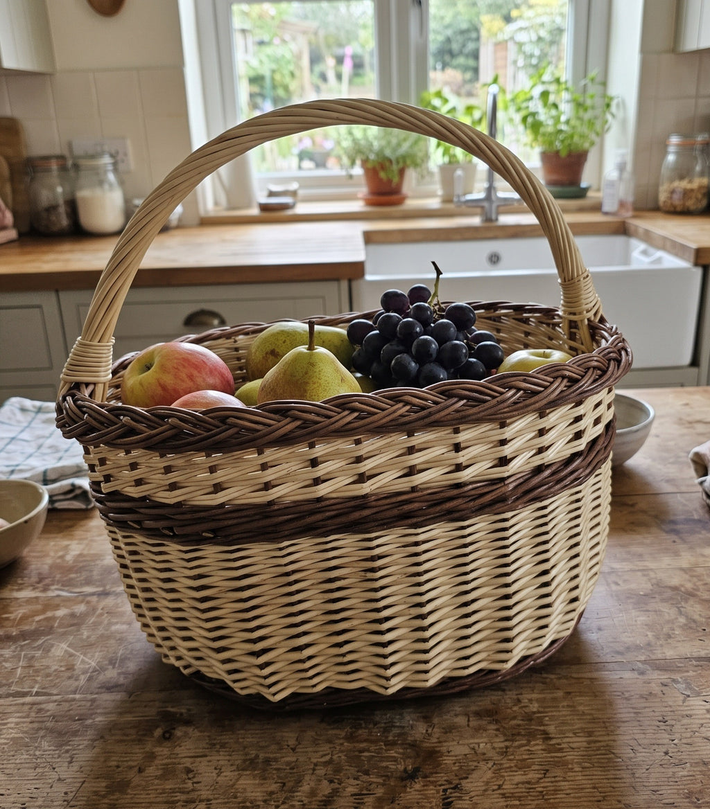 Handwoven willow basket with handle filled with apples, pears and grapes on a farmhouse kitchen counter by the sink and window.