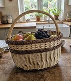 Handwoven willow basket with handle filled with apples, pears and grapes on a farmhouse kitchen counter by the sink and window.