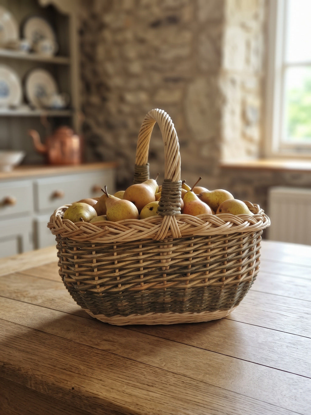 Small oval willow basket with handle holding ripe pears on a farmhouse kitchen table in a stone cottage