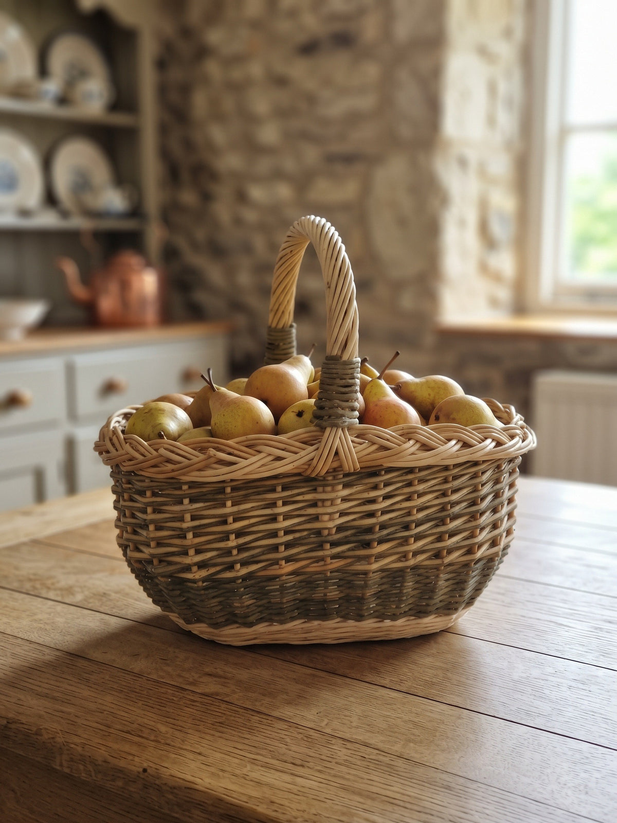 Small oval willow basket with handle holding ripe pears on a farmhouse kitchen table in a stone cottage
