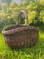Close view of the small willow basket with a braided rim and an arched handle on the lawn in front of hydrangeas