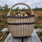 Egg gathering basket with tall handle filled with porcini mushrooms, a deep oval wicker willow basket on a wooden boardwalk in a bog.