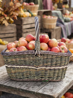 Großer Marktkorb mit gedrehtem Henkel voller roter Äpfel auf einem rustikalen Tisch beim herbstlichen Bauernmarkt