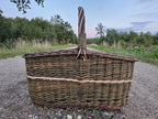 Seitenansicht des großen Holzkorbs mit hohem, aufrechtem Henkel auf einem Schotterweg unter dem Abendhimmel