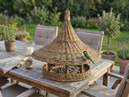 Willow bird feeder with a wide woven brim on a wooden patio dining table, with a great tit perched on the roof edge