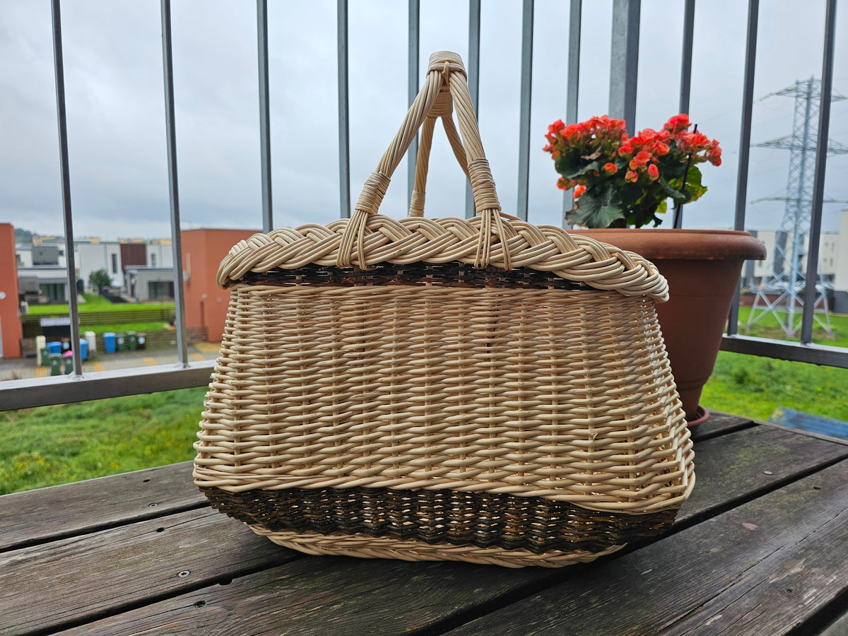 Side view of the handwoven willow garden basket with two handles and thick braided rim on a balcony table.