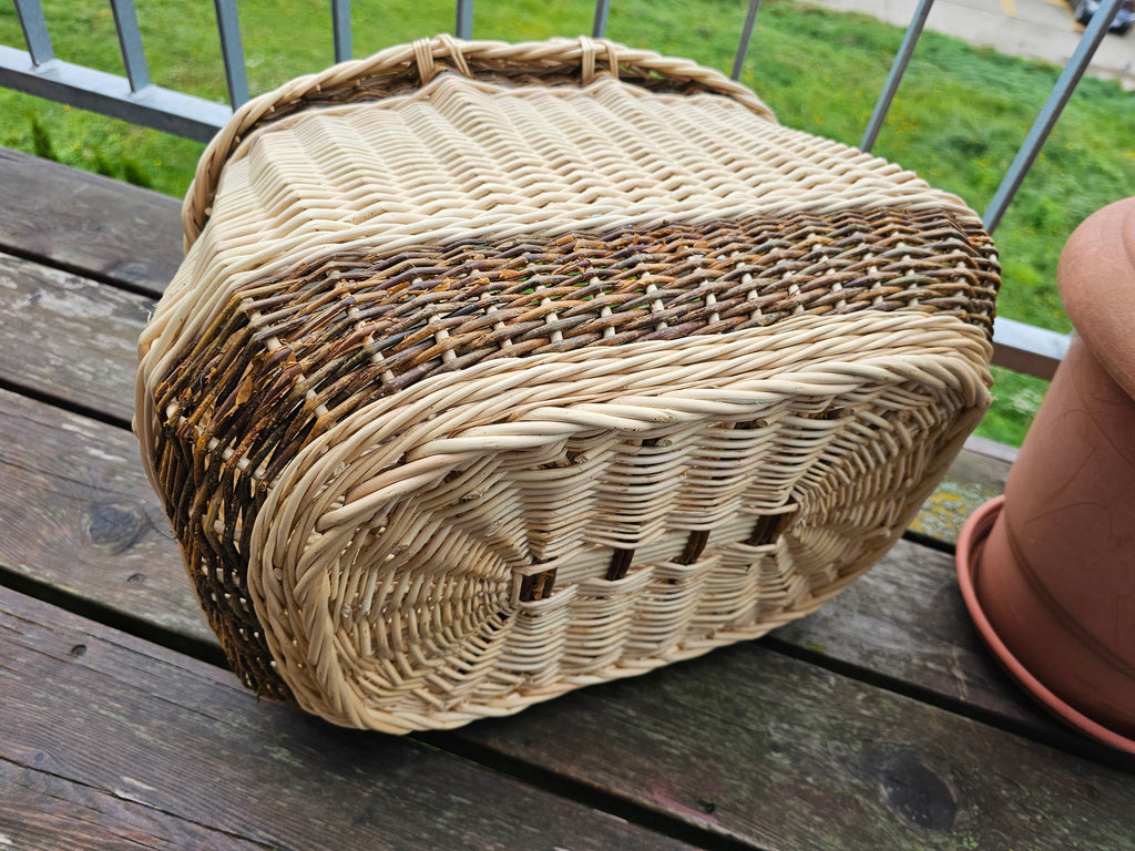 Underside of the willow garden basket with two handles lying on its side, showing the sturdy woven base on a wooden table.