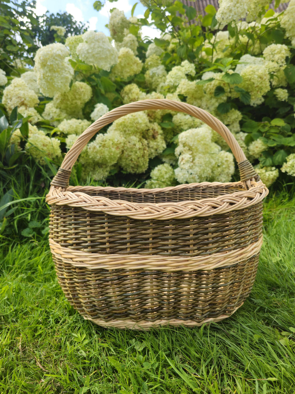 Wicker basket on grass with a background of green foliage and white flowers