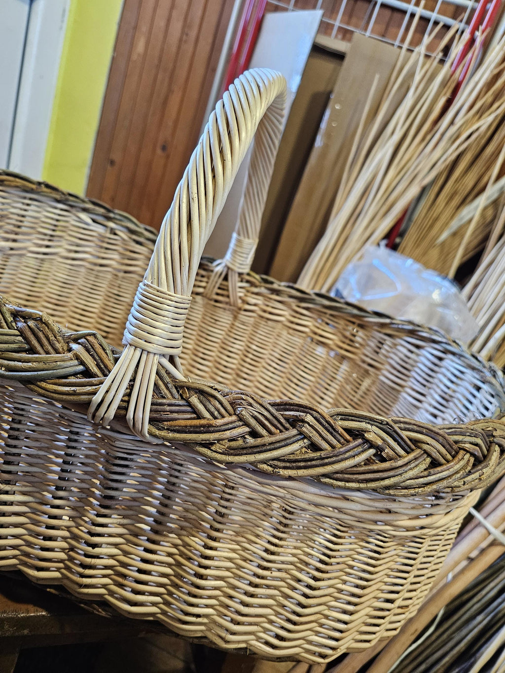 Close-up of the large wicker market basket showing the thick braided rim and the handle bound with willow wraps