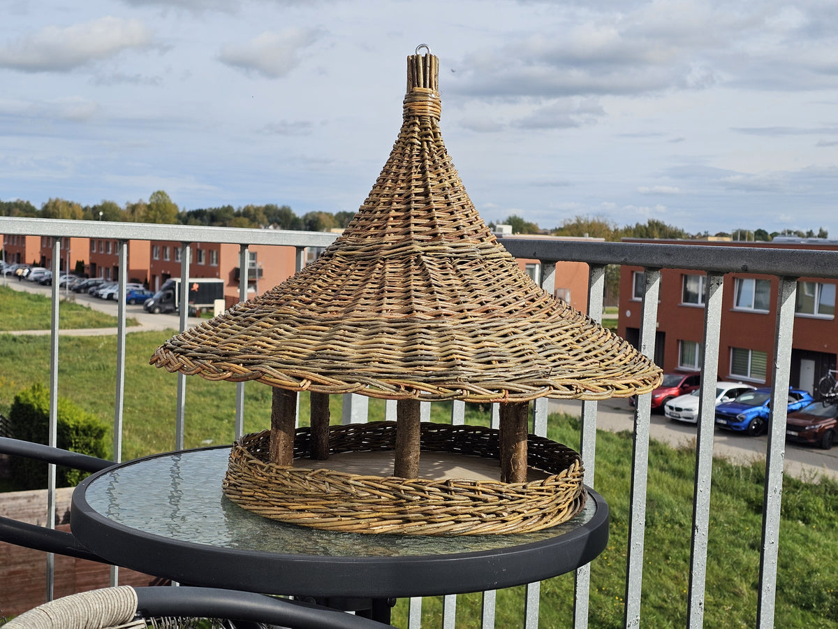 Extra large pagoda roof bird feeder on a balcony table, wide woven brim covering the whole feeding platform