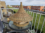 Front view of the handwoven willow bird feeder with tall pointed roof on a round glass table outdoors
