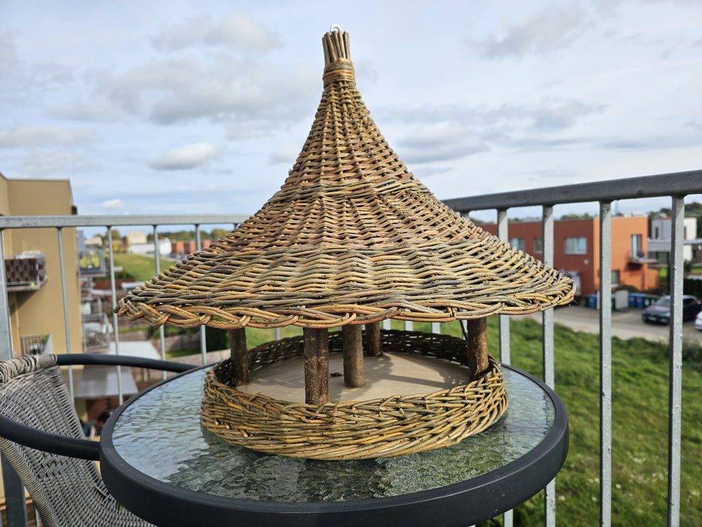 Willow bird feeder on a glass garden table, the wide woven roof brim above the open feeding platform