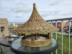 Willow bird feeder on a glass garden table, the wide woven roof brim above the open feeding platform