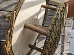 Close-up of bark-on branch posts fixed between the wooden roof disc and the wooden platform of the willow bird feeder