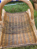 Close-up looking down into the wicker firewood trug, showing the open weave of the floor and the tall tightly twisted handle