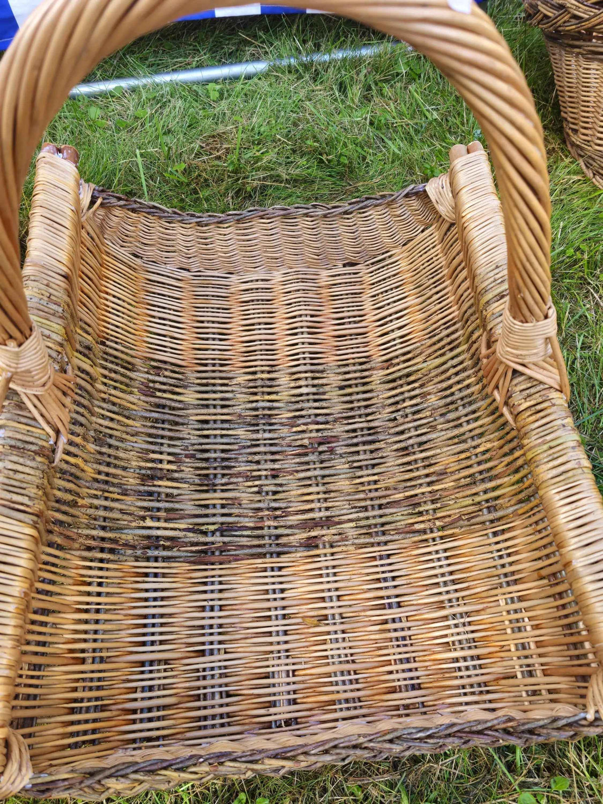 Close-up looking down into the wicker firewood trug, showing the open weave of the floor and the tall tightly twisted handle