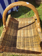 Close-up of the rectangular willow log carrier with a thick twisted handle, showing the woven floor and the reinforced long sides