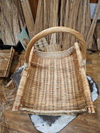 Handwoven willow firewood basket with rolled willow edges and a twisted handle, photographed in the Lithuanian workshop where it was woven.