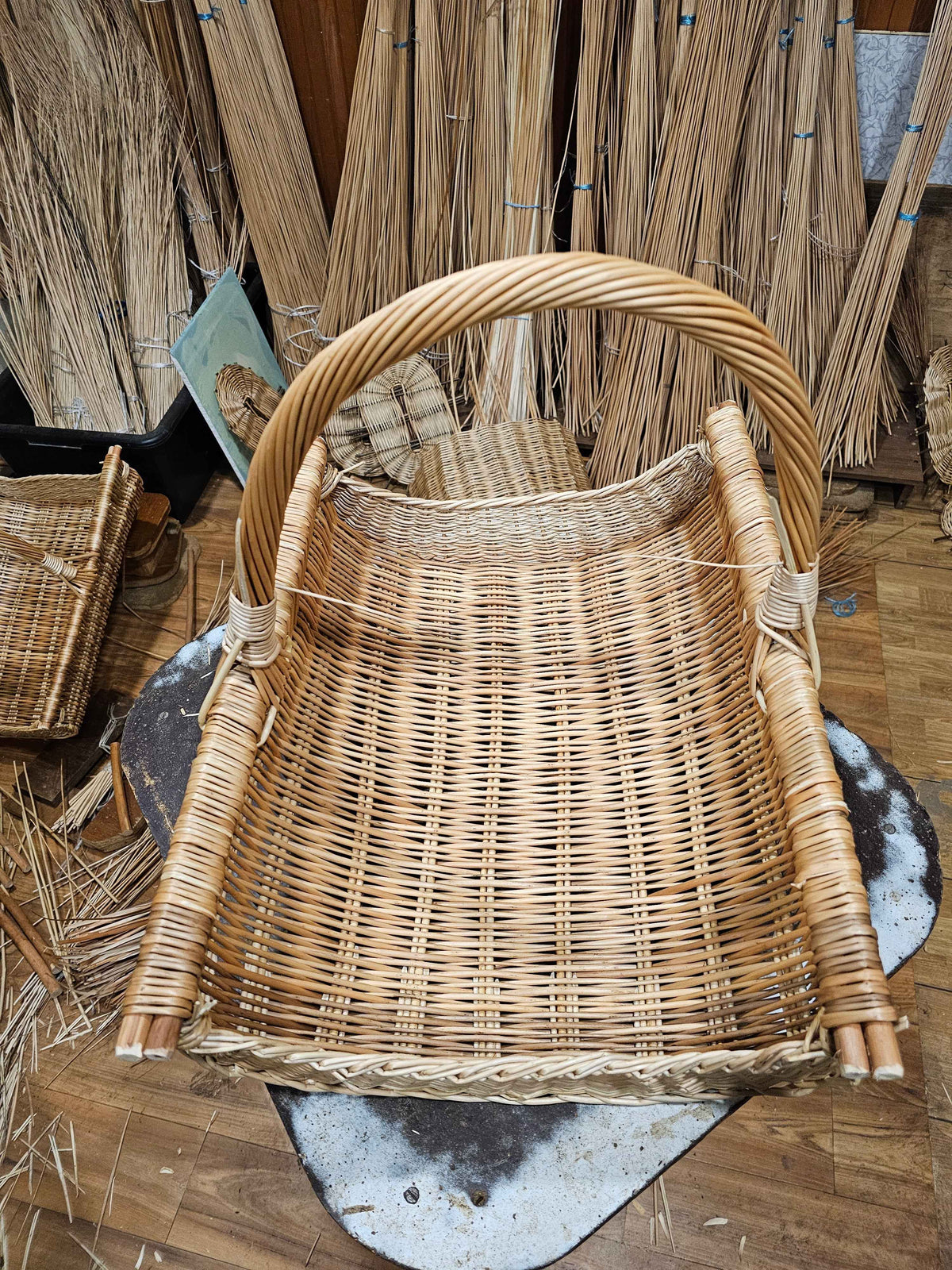 Handwoven willow firewood basket with rolled willow edges and a twisted handle, photographed in the Lithuanian workshop where it was woven.