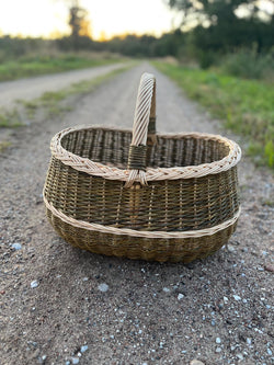 Großer Marktkorb mit Zopfrand und Bügelhenkel auf einem Schotterweg in der Abenddämmerung