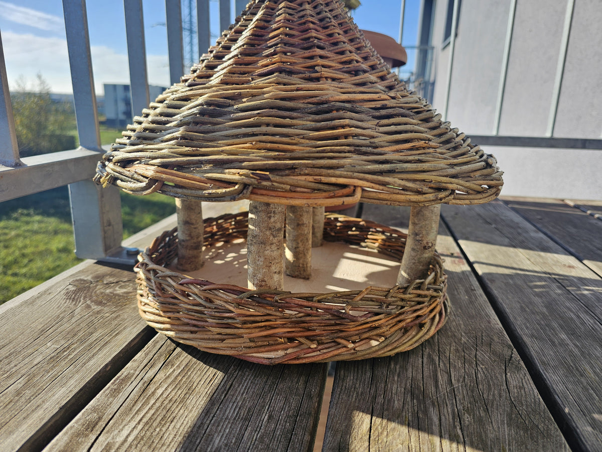 Vogelfutterhaus aus Weide aus der Nähe auf dem Holzboden des Balkons: Kegeldach und offene Futterschale