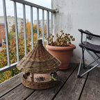 Vogelfutterhaus aus Weide mit Kohlmeise auf dem Balkonboden neben einer Topfpflanze