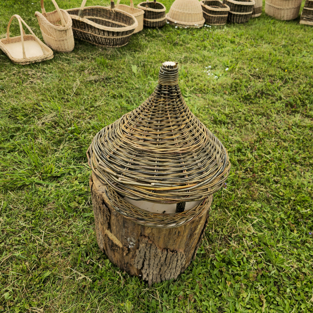 Wicker bird feeder standing on a log on the grass, with handwoven baskets behind