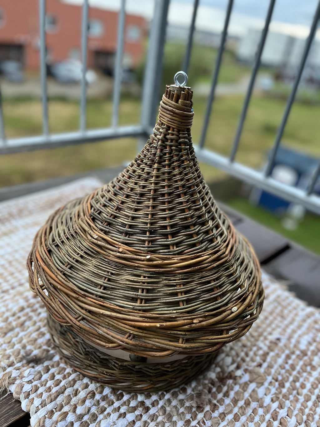 Willow bird feeder with cone roof on a woven rug on a balcony table