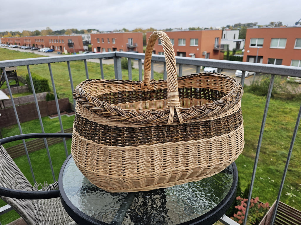 Large oval willow basket with braided rim on a round glass table on a balcony