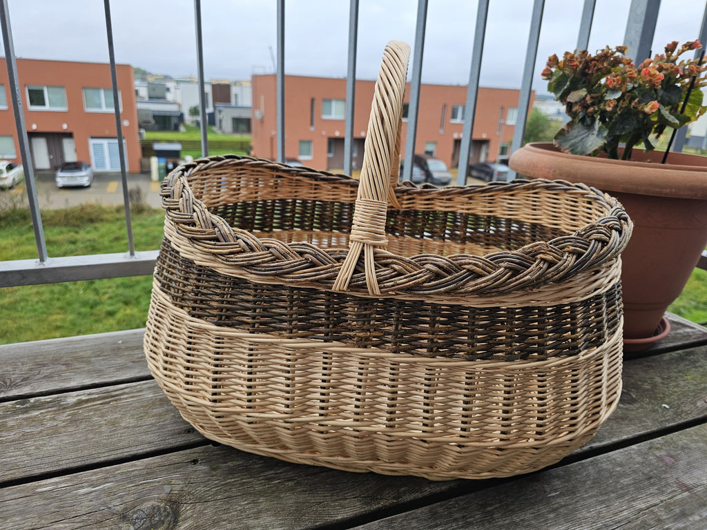 Large oval willow basket on a wooden balcony table beside a flower pot