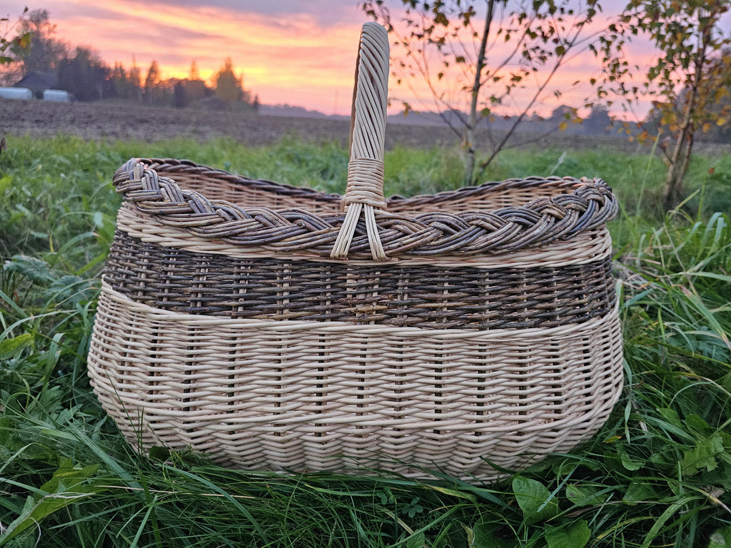 Großer ovaler Weidenkorb mit Zopfrand aus ungeschälter Weide auf einem Feld bei Sonnenuntergang