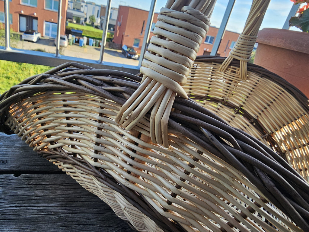 Close-up of the tall handle bound tightly into the rim of the large willow gathering trug, on a wooden balcony table