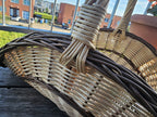Close-up of the tall handle bound tightly into the rim of the large willow gathering trug, on a wooden balcony table