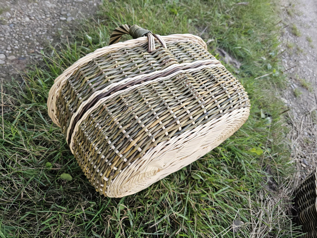 Wicker market basket tipped on its side in the grass to show the woven base and the foot rim underneath