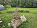 Hanging willow bird table with a conical roof placed on split logs in a mown meadow, showing its full height and woven tray rim