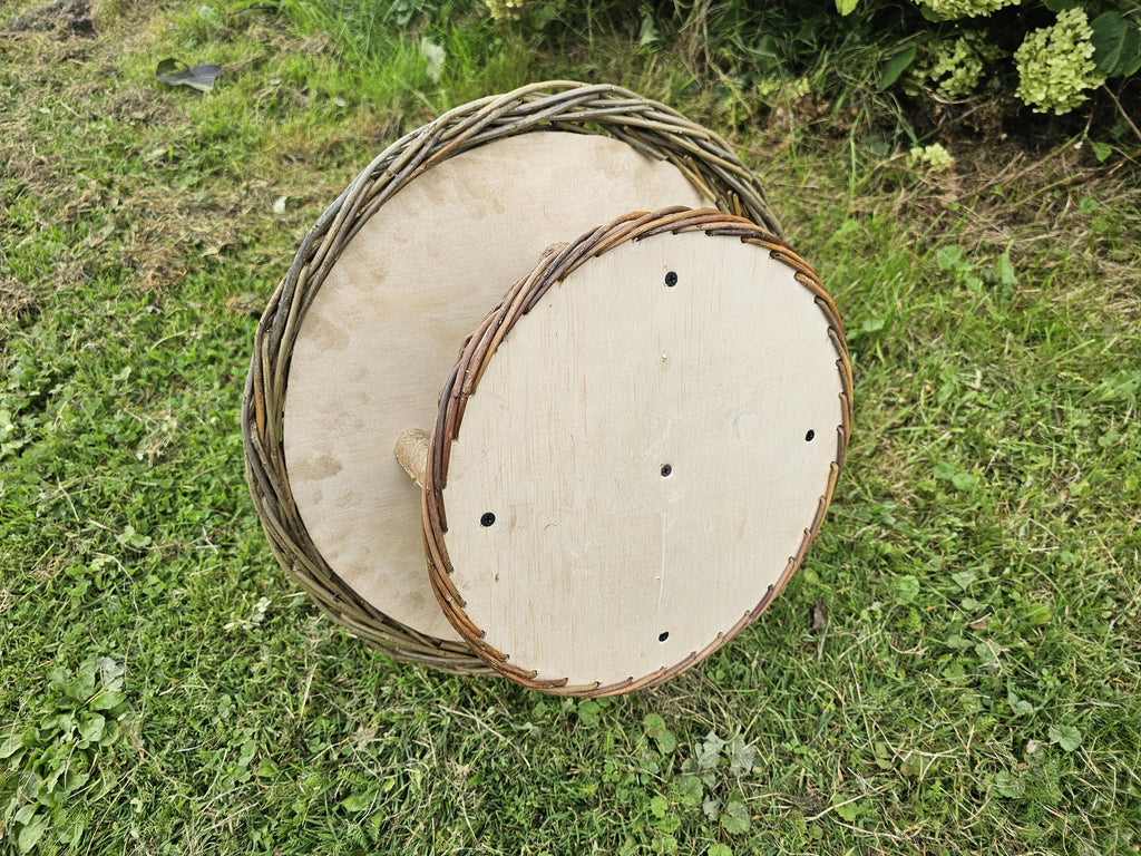 Underside of the round wooden seed platform with small drainage holes and the woven willow rim of the hanging bird table