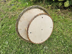 Underside of the round wooden seed platform with small drainage holes and the woven willow rim of the hanging bird table