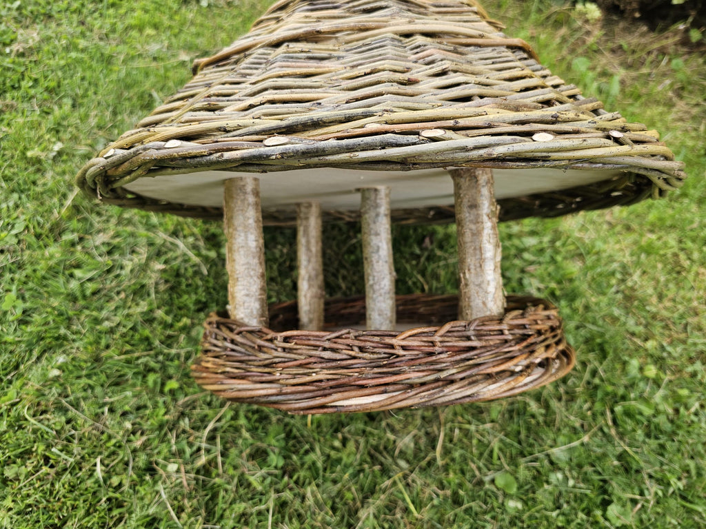 Close-up of the branch posts holding the conical willow roof above the wooden seed tray framed by a thick woven rim