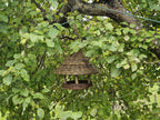 Willow hanging bird table with a conical roof suspended from the branch of an apple tree among green leaves in the garden