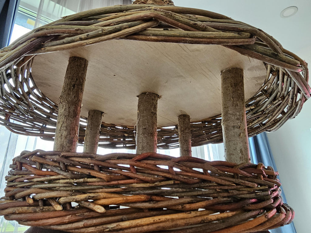 Close view under the roof of the willow bird table showing the wooden branch posts, the underside of the roof and the woven tray rim